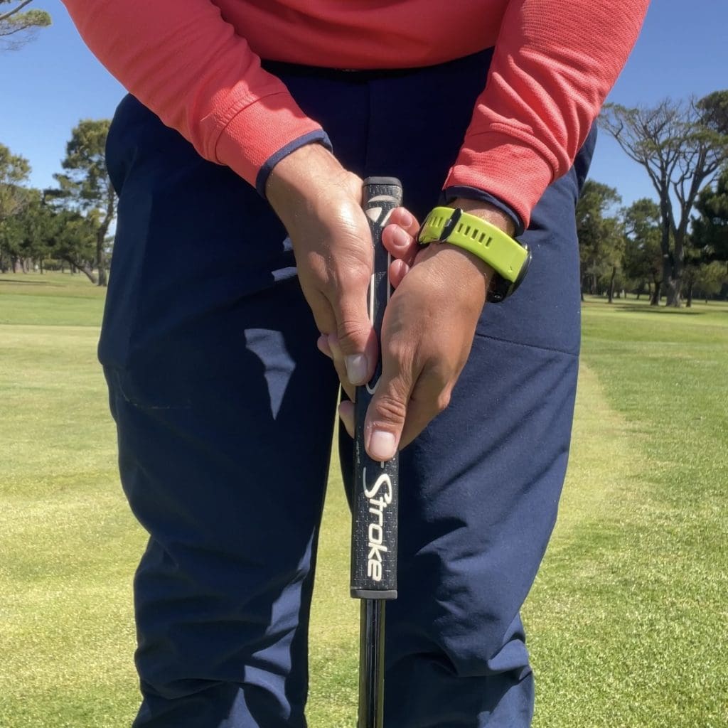 Golfers hands holding putter in unconventional putting grip with left-hand low.