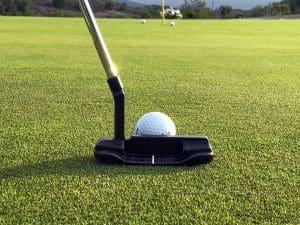 View from behind of putter and golf ball with flag in the distance.